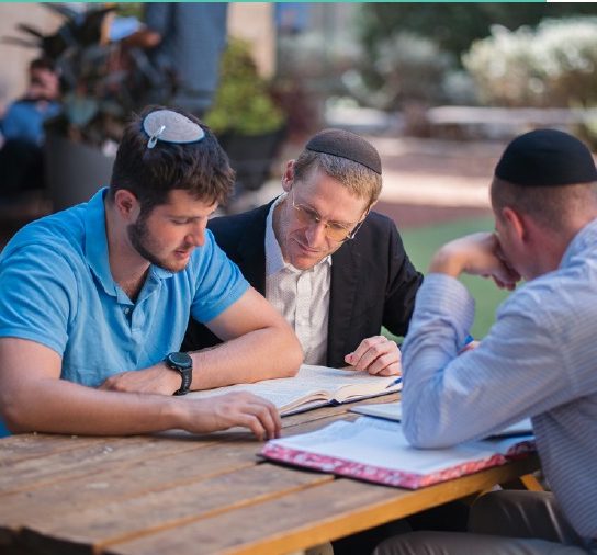 Three talmidim learning at an outdoor table on campus